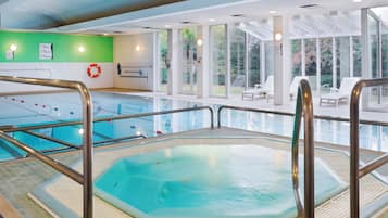 Una piscina interior con un jacuzzi, señales de seguridad y una zona soleada con sillones de descanso.