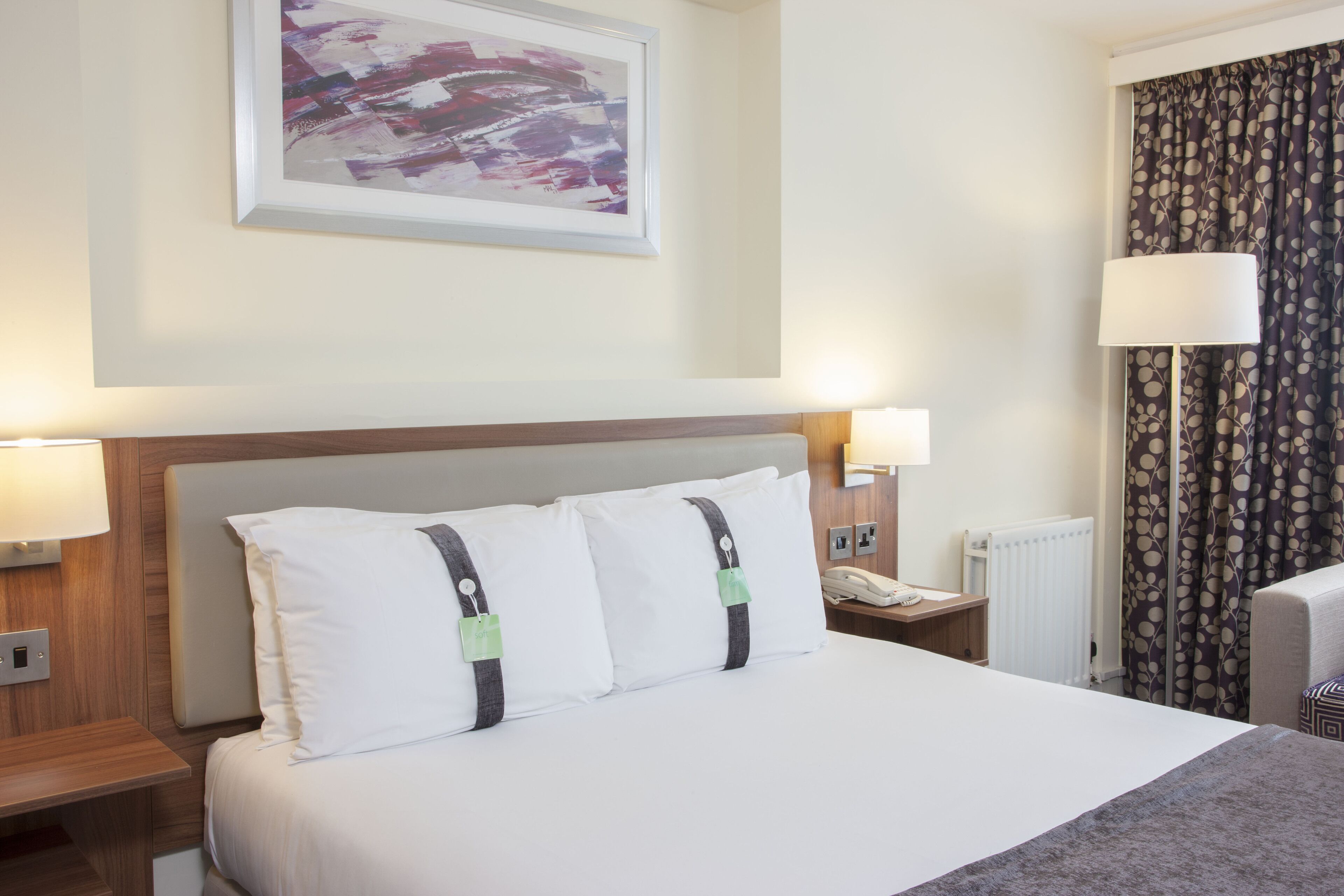 A hotel room with a large bed, two bedside lamps, a telephone, and a radiator.