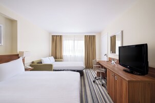 Habitación de hotel con dos camas, un escritorio con televisor, una silla y una ventana con cortinas.
