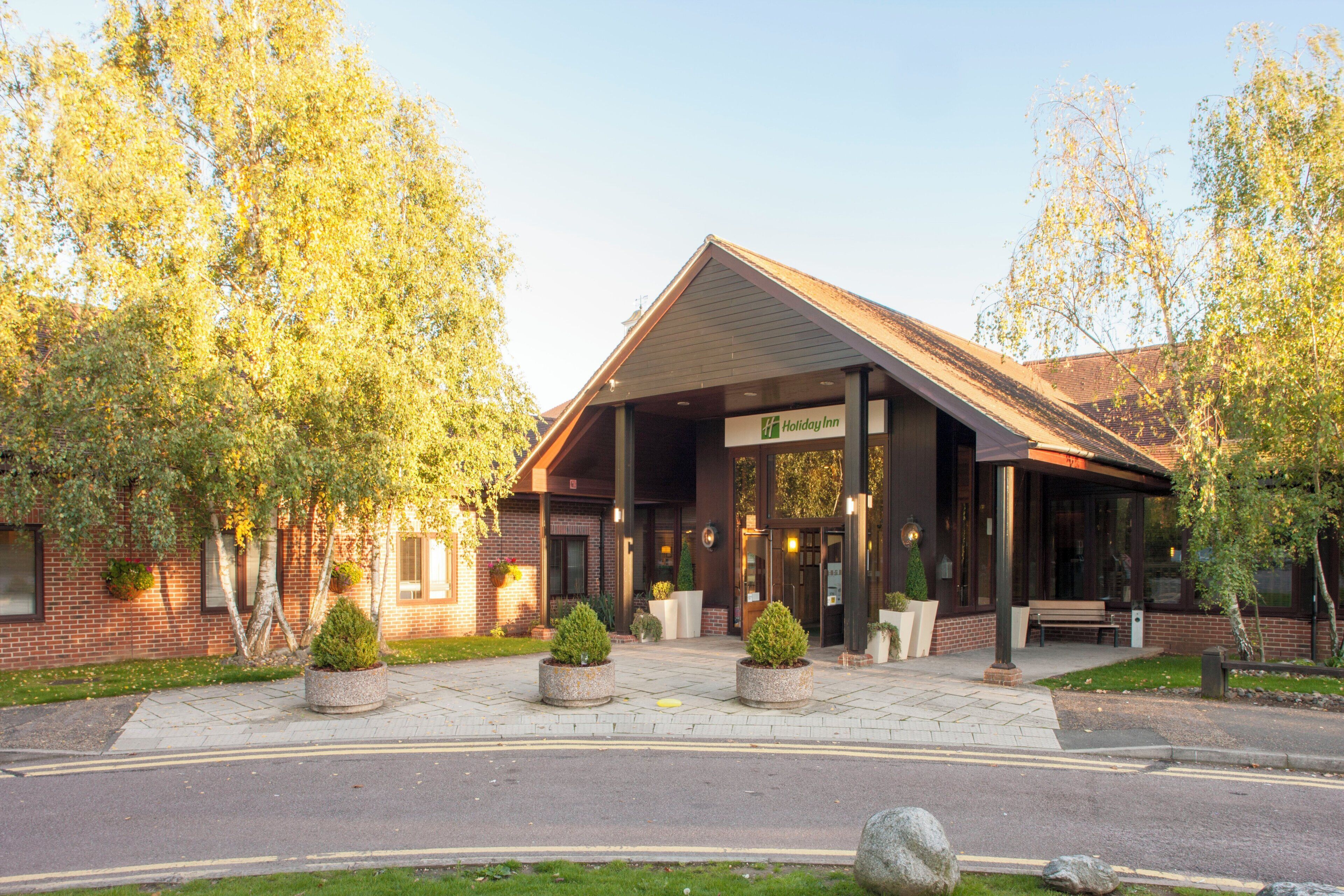 A Holiday Inn with a brick facade, a covered entrance, and a landscaped front yard with planters and a bench.