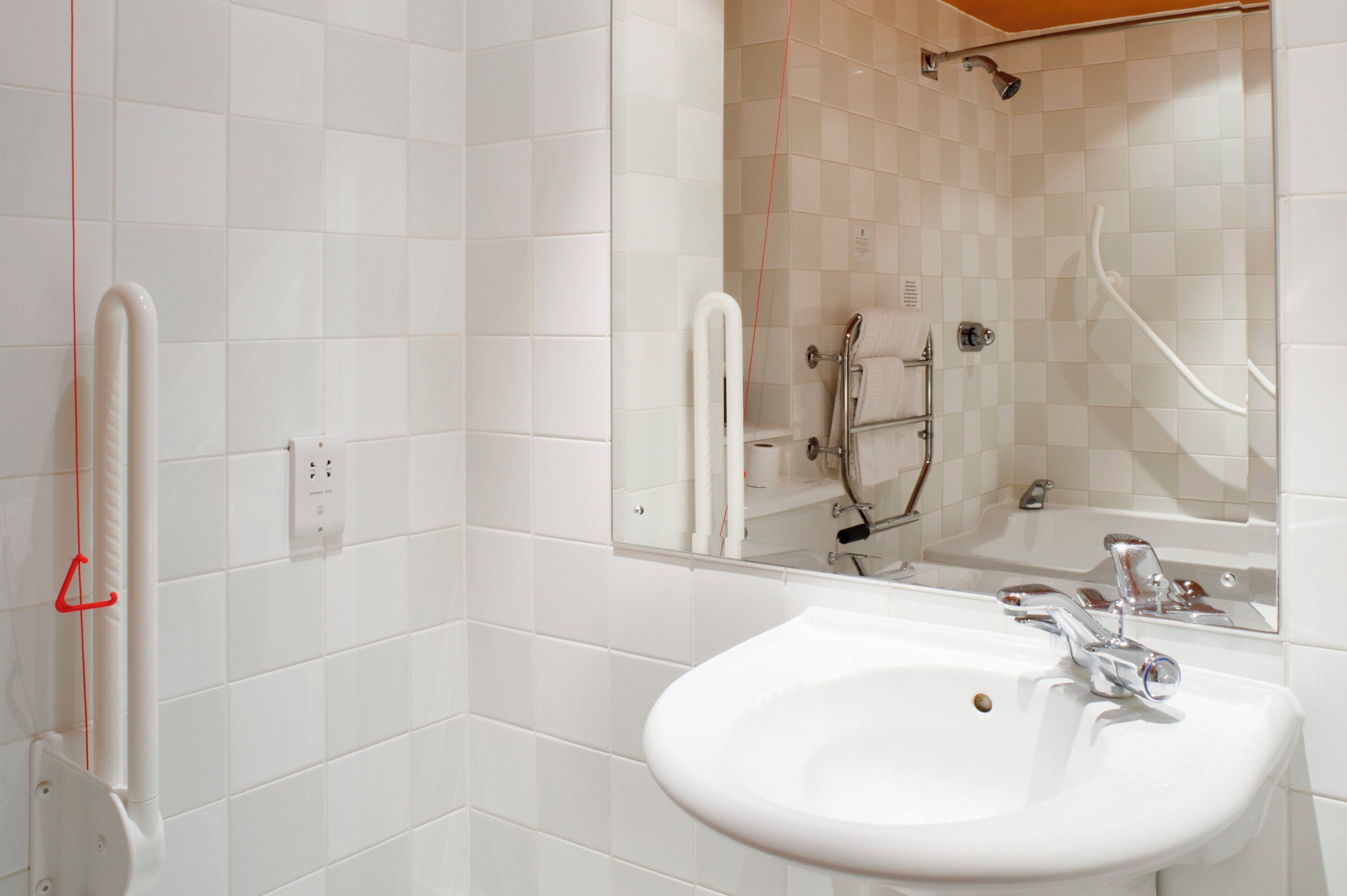 A bathroom with white tiles, a sink, a mirror, and a shower area.