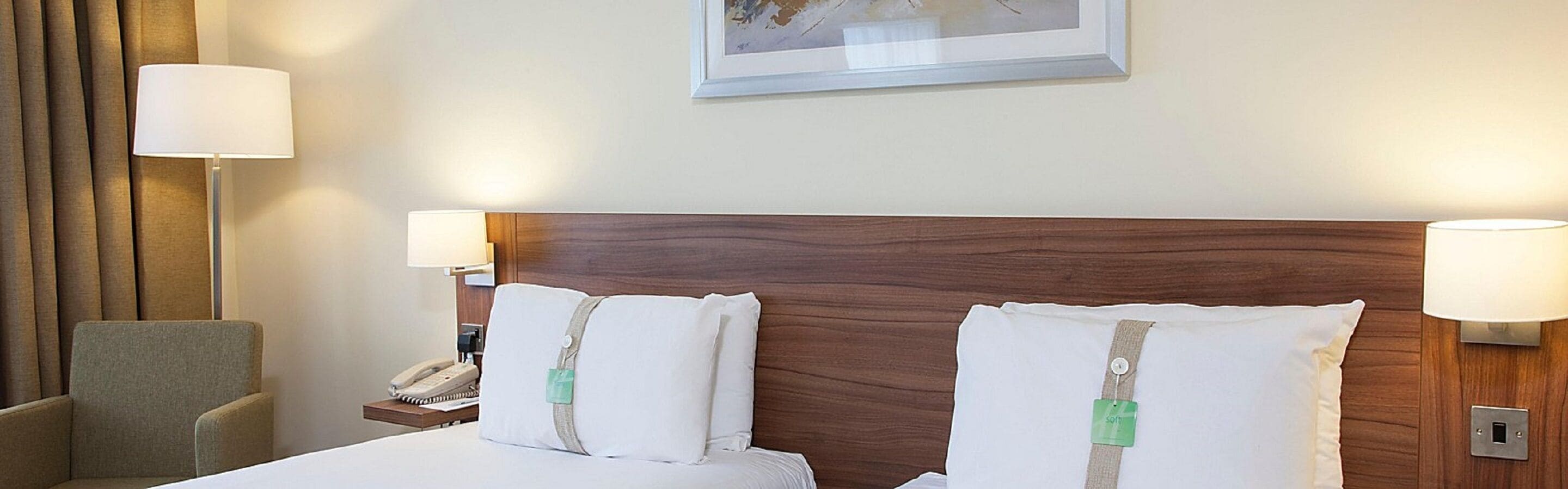 Una habitación de hotel con cabecera de madera, dos lámparas de noche, un teléfono y una silla.