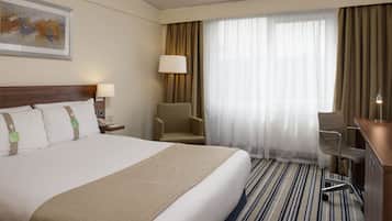 Una habitación de hotel con una cama grande, un escritorio, una silla, una lámpara y una ventana con cortinas.