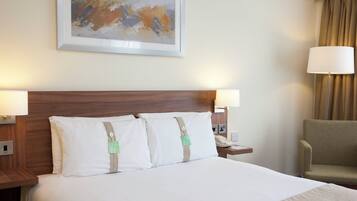 A hotel room with a large bed, two bedside lamps, a nightstand with a phone, a chair, and a painting on the wall.