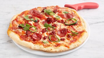 Una pizza con pepperoni, jalapeños y queso sobre un plato blanco.