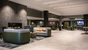A modern lobby with a fireplace, seating area, and a television screen displaying a news program. - West Des Moines Marriott (West Des Moines)