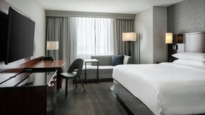 A hotel room with a large bed, a desk with a flat-screen TV, a chair, a small table, and two bedside lamps. - West Des Moines Marriott (West Des Moines)