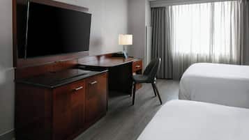 A hotel room with a large flat-screen TV mounted on the wall, a desk with a lamp, a chair, and two beds.