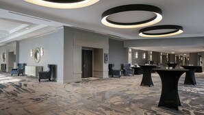 A spacious hotel lobby with a carpeted floor, round ceiling lights, and several tables and chairs. - West Des Moines Marriott (West Des Moines)