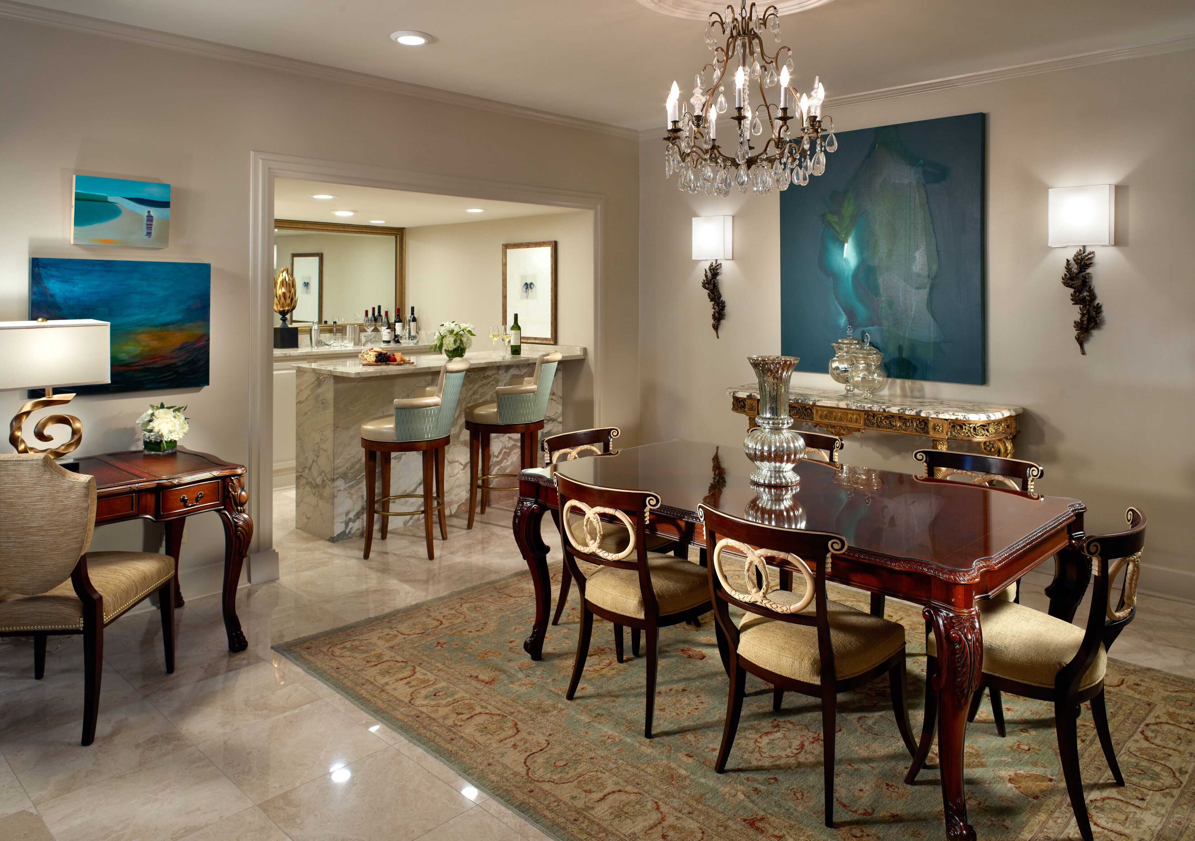 A dining area with a marble floor, a chandelier, and a large painting on the wall.