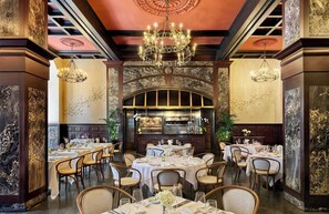 A restaurant with round tables, chandeliers, and a stone archway. - Omni Royal Orleans Hotel (New Orleans)
