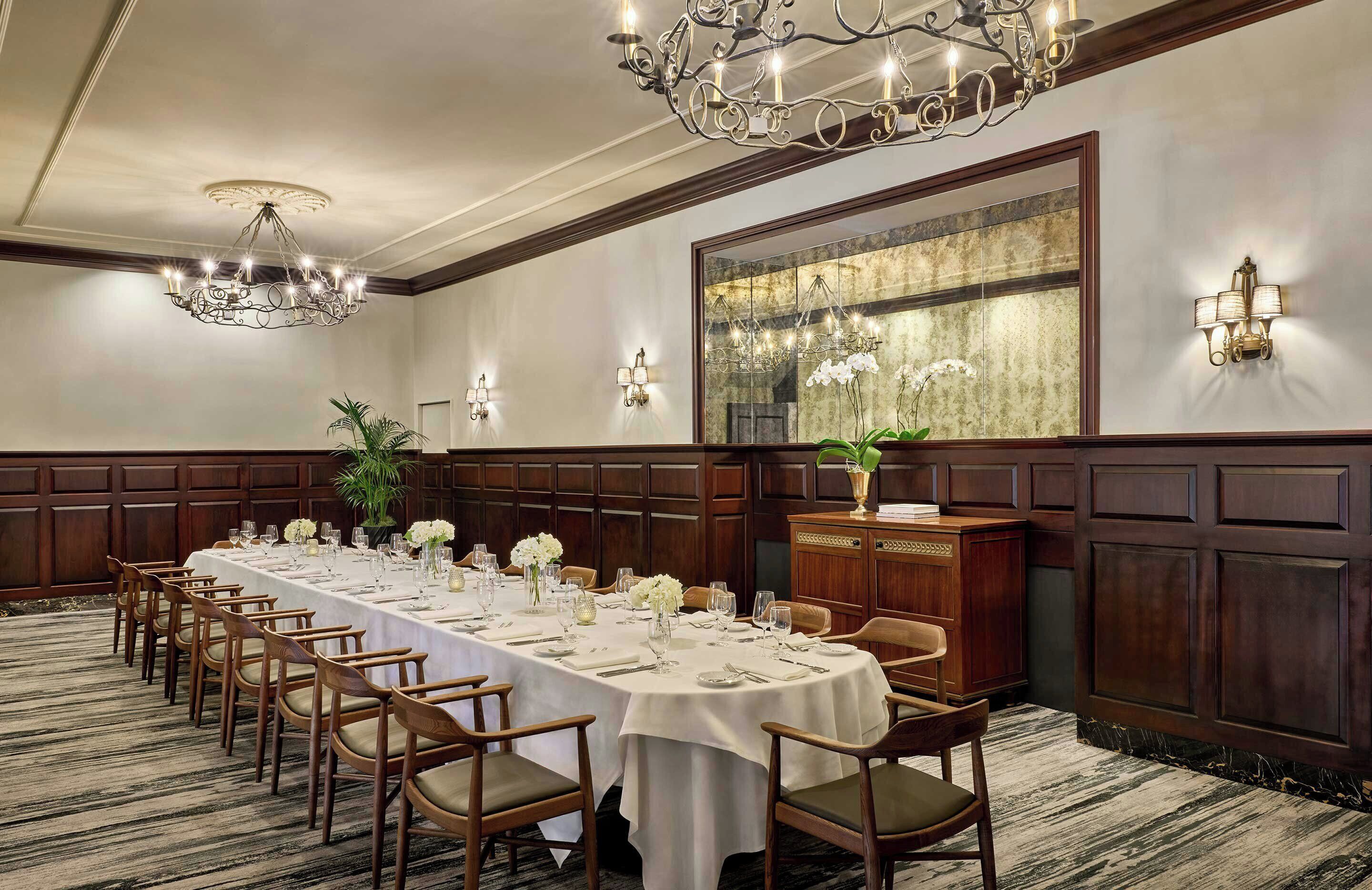 Ein langer Bankettisch, gedeckt für eine festliche Veranstaltung, mit einer Chandelier, Wandleuchtern und einem großen Spiegel.