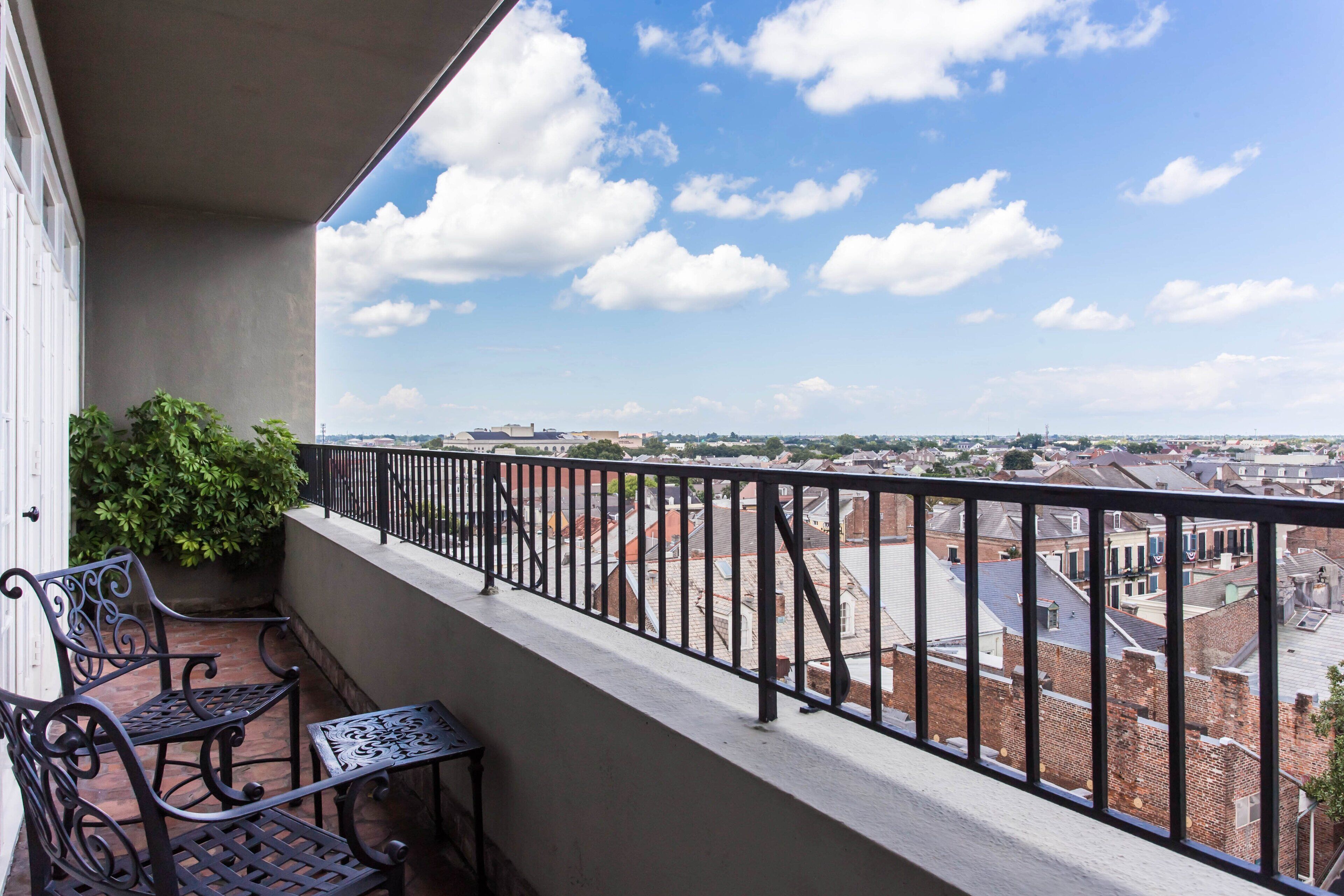 Un balcon donnant sur un paysage urbain, avec une balustrade, un pot de fleurs et deux chaises en métal.