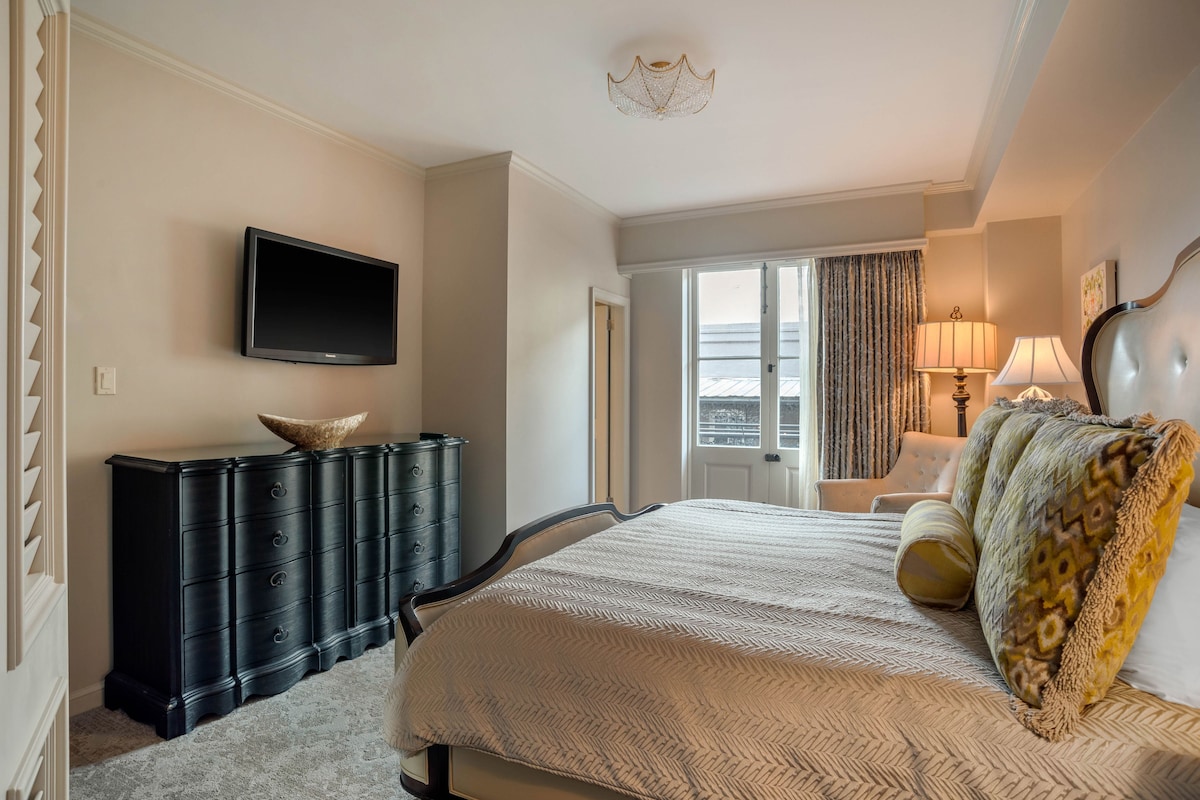 Une chambre d’hôtel avec un lit, une commode, une télévision et une fenêtre avec des rideaux.