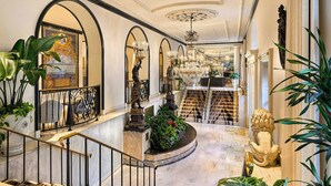 Eine prächtige Hotelhalle mit Marmorböden, aufwendigen Kronleuchtern und einer Treppe mit schwarzen Geländern.