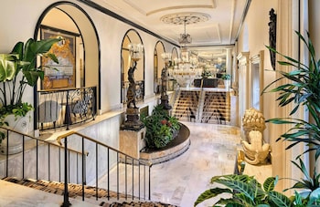 A balcony with a table and chairs, a vase of flowers, and a view of a classical building. at Omni Royal Orleans Hotel