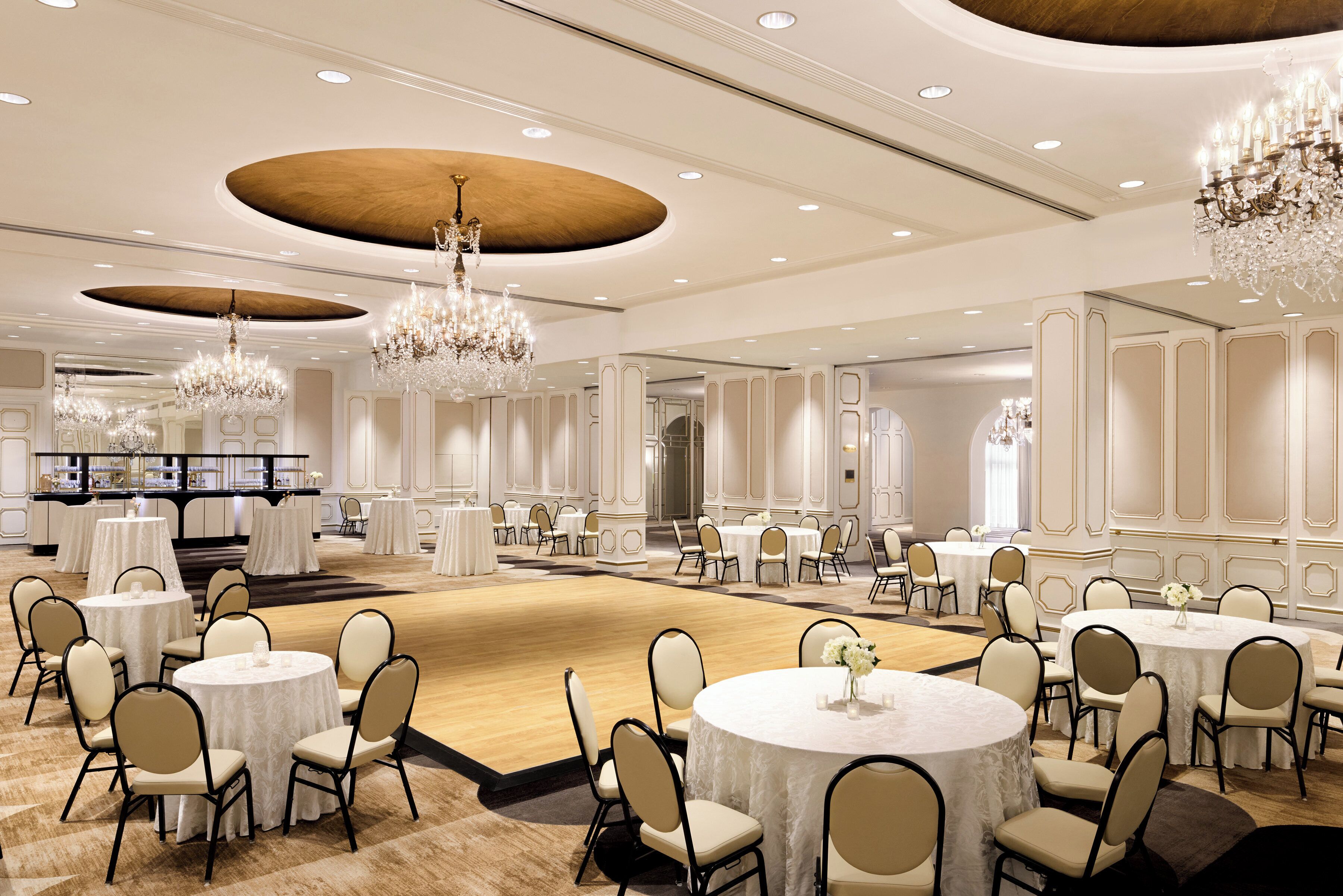 Une vaste salle de banquet dotée de tables et de chaises rondes, de lustres et d’un plafond en bois.