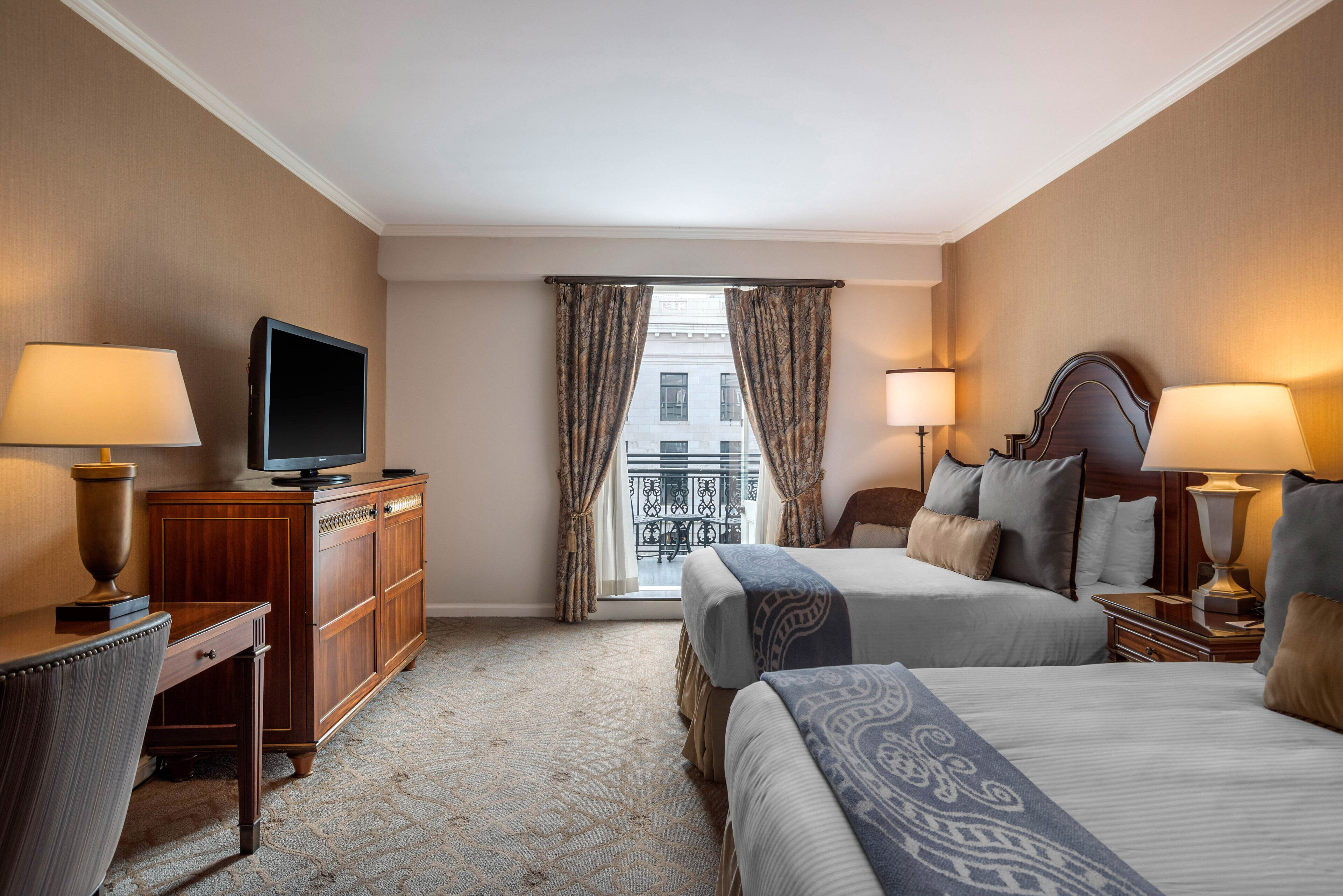 Quarto de hotel com duas camas, televisão, escrivaninha e janela com cortinas.