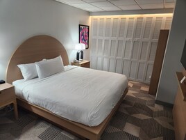 Quarto de hotel com uma cama grande, mesa de cabeceira com abajur, telefone e televisão na parede.