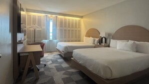 Habitación de hotel con dos camas, un escritorio y vistas al exterior.
