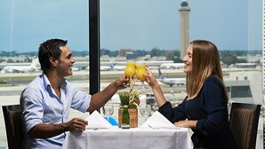 Una pareja sentada en una mesa con vista a un aeropuerto y una torre al fondo.