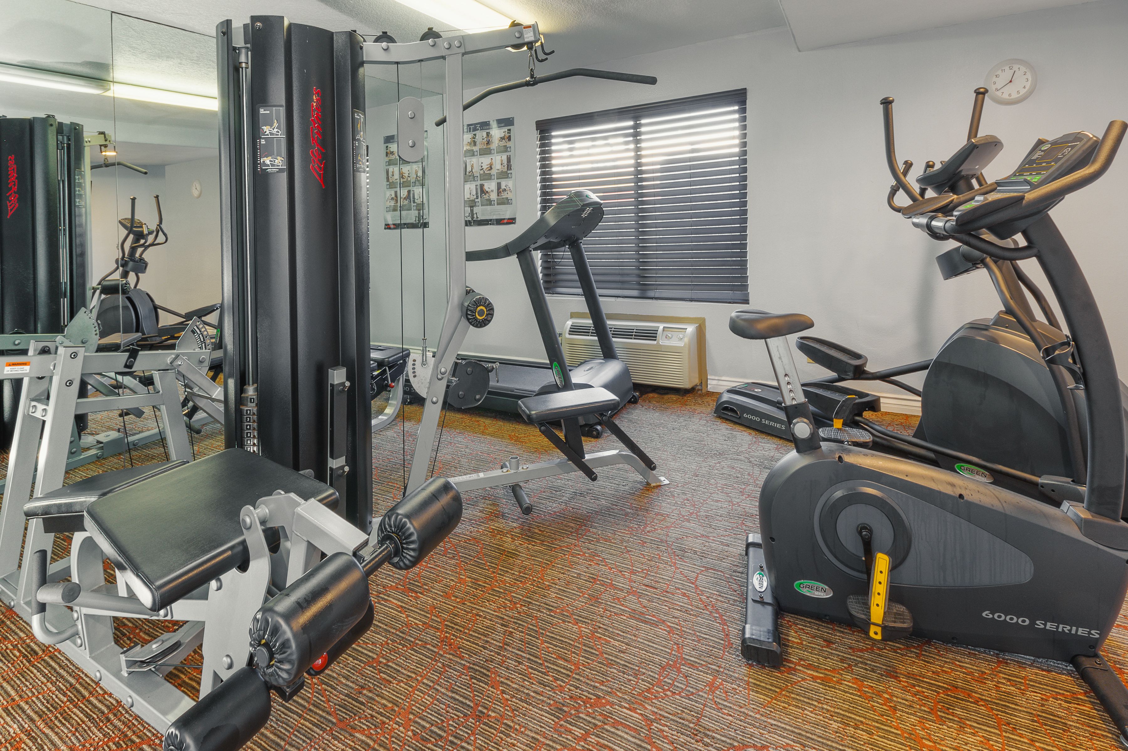 A gym with exercise equipment, a mirror, and a window with blinds.
