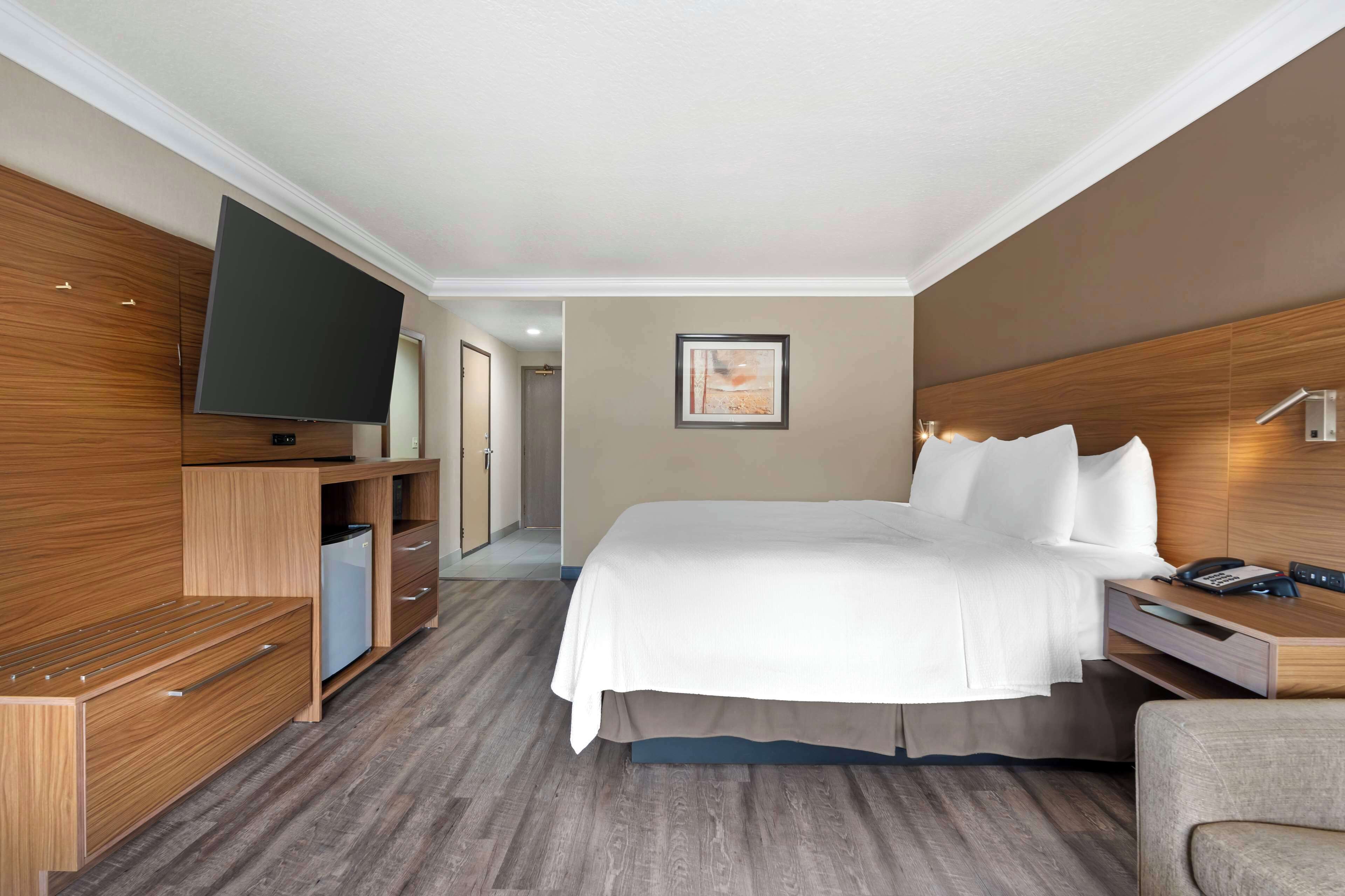 Une chambre d’hôtel dotée d’un grand lit, d’un téléviseur à écran plat fixé au mur, d’une commode en bois et d’un petit coin salon.