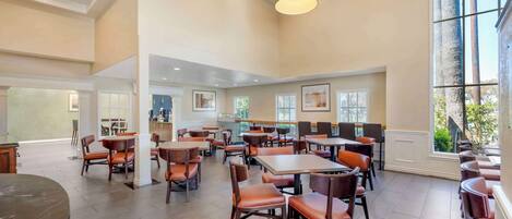 A spacious dining area with multiple tables and chairs, large windows, and ceiling lights.