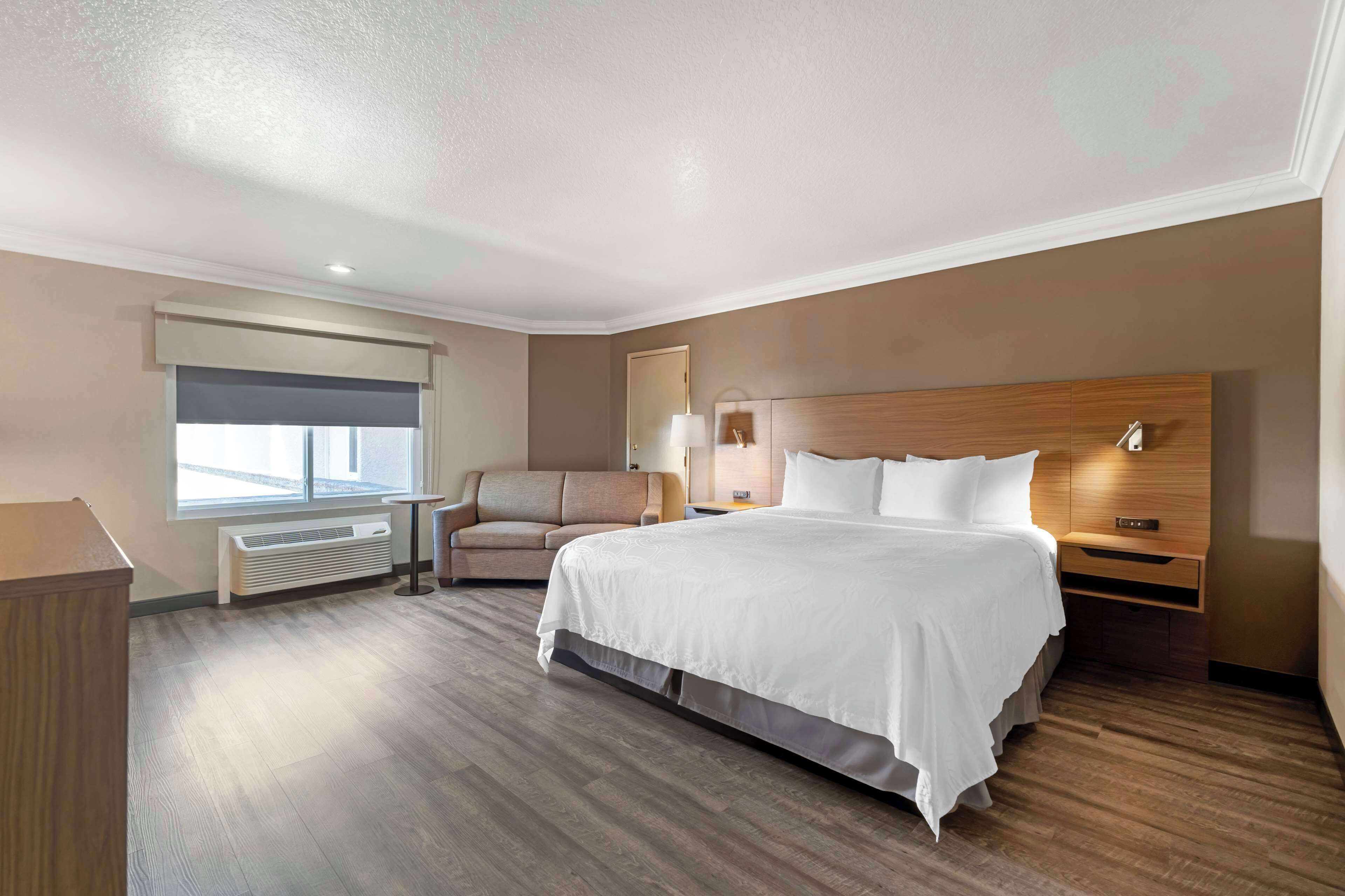 Quarto de hotel com uma cama grande, um sofá, uma escrivaninha e uma janela com persianas.