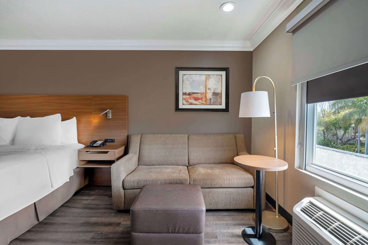 Une chambre d’hôtel avec un lit, un canapé, une petite table, une lampe et une fenêtre donnant sur un beau paysage.
