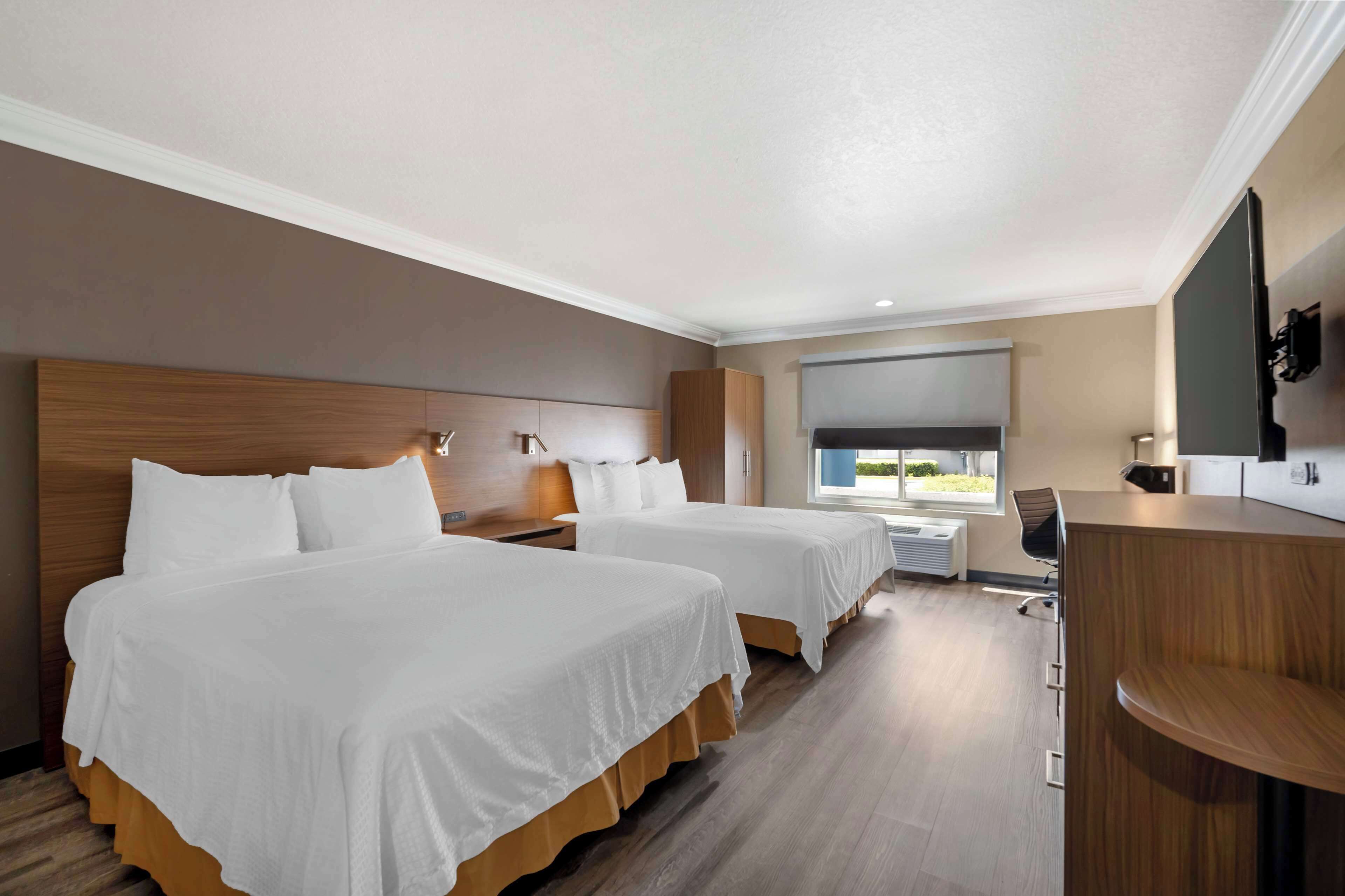 A hotel room with two beds, a desk, a chair, a TV, and a window with a view.
