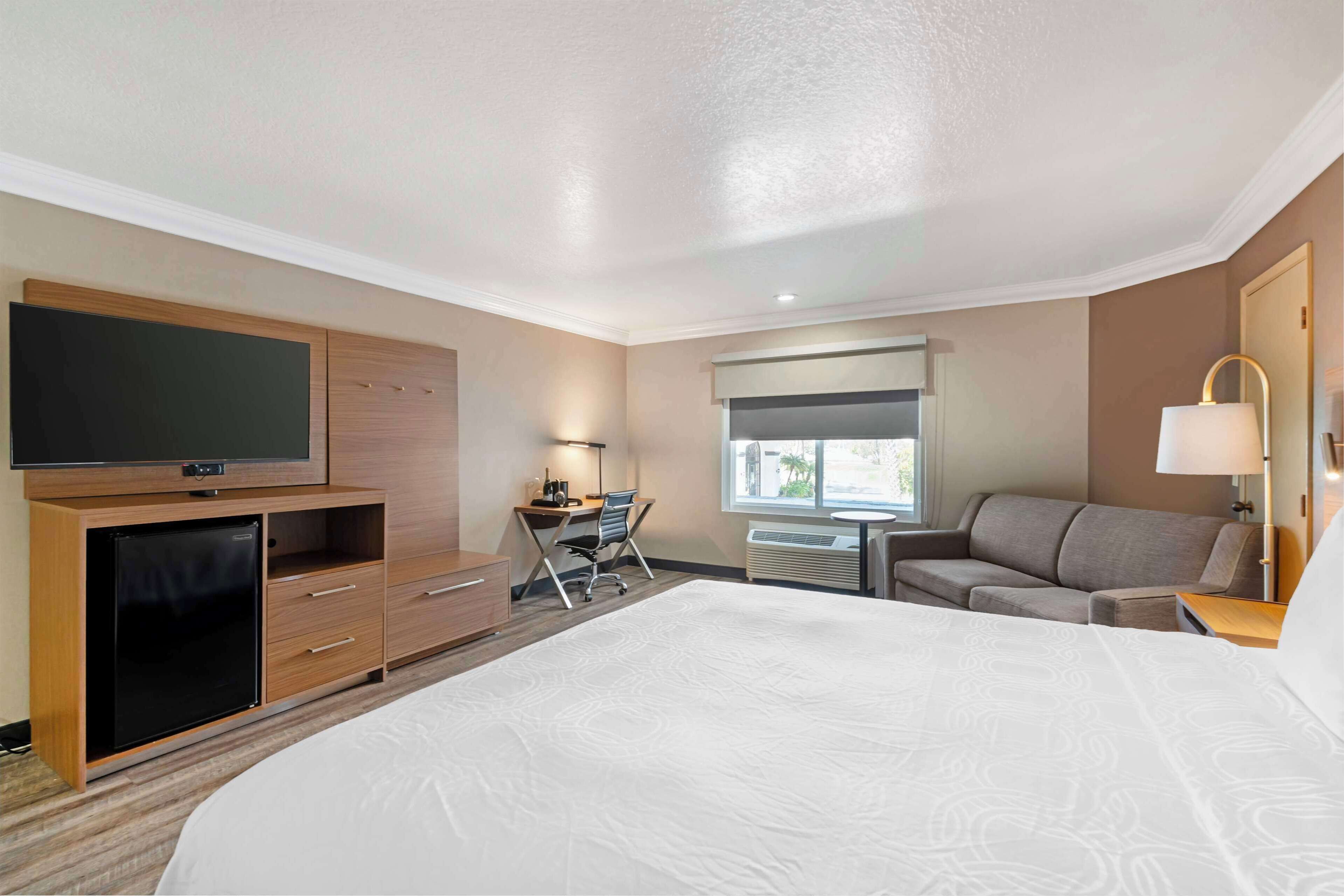 Une chambre d’hôtel avec un grand lit, un bureau avec une chaise, une télévision, un canapé et une fenêtre.
