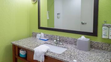 A bathroom with a granite countertop, a sink, a mirror, a towel, a soap dispenser, and a hand dryer.