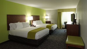Quarto de hotel com duas camas, uma escrivaninha, uma cadeira, uma televisão e uma janela com cortinas.