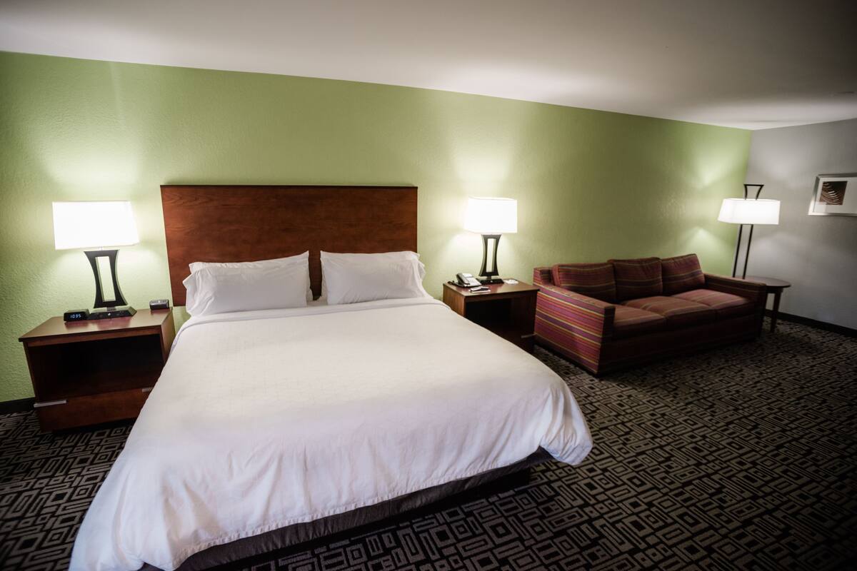 A hotel room with a large bed, two bedside tables with lamps, a sofa, and a patterned carpet.