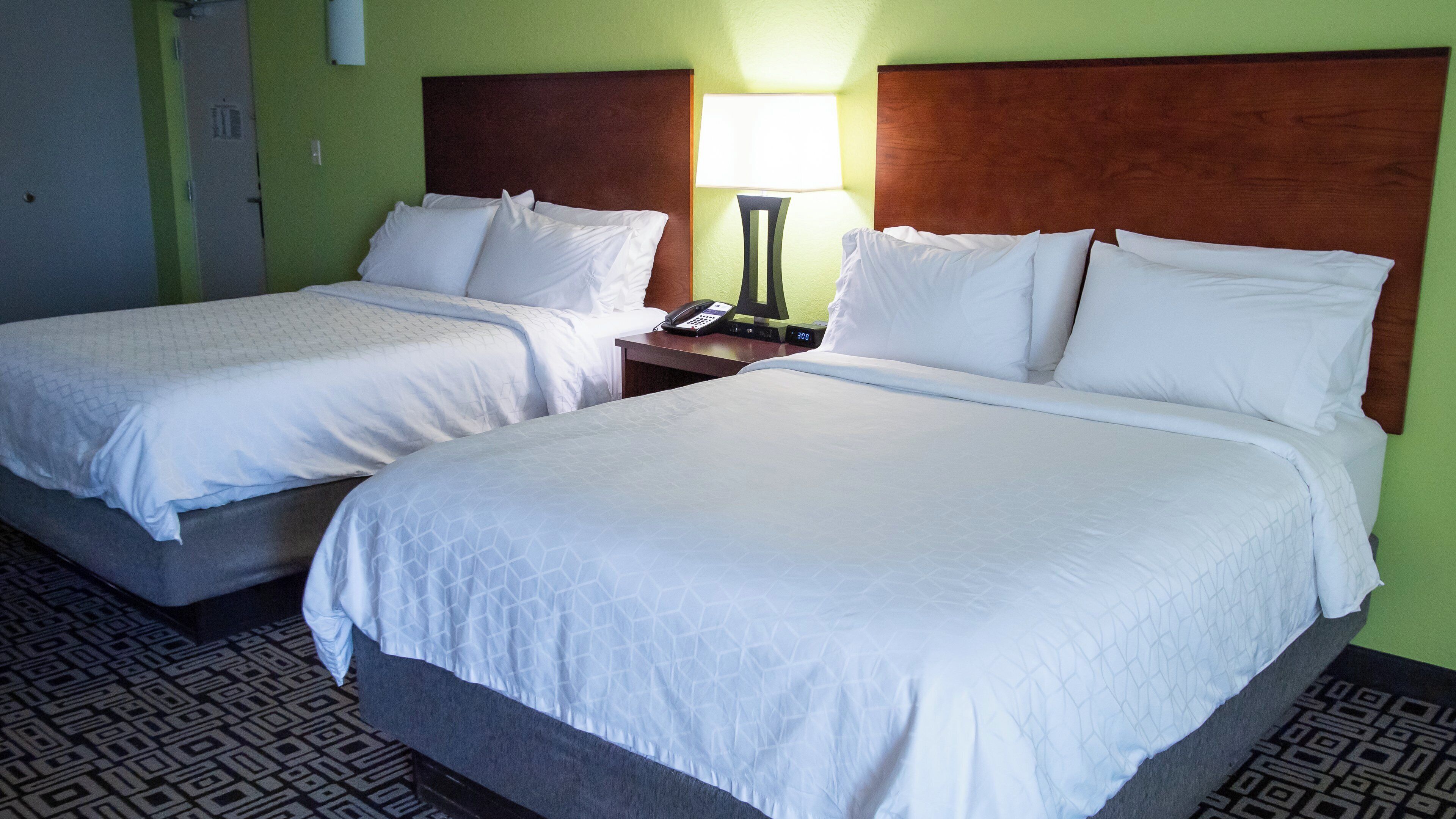Una habitación de hotel con dos camas individuales, una mesita de noche con lámpara y un teléfono.