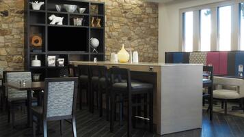 Un interior moderno con una pared de piedra, una estantería negra con varios objetos decorativos y una zona de bar con asientos.