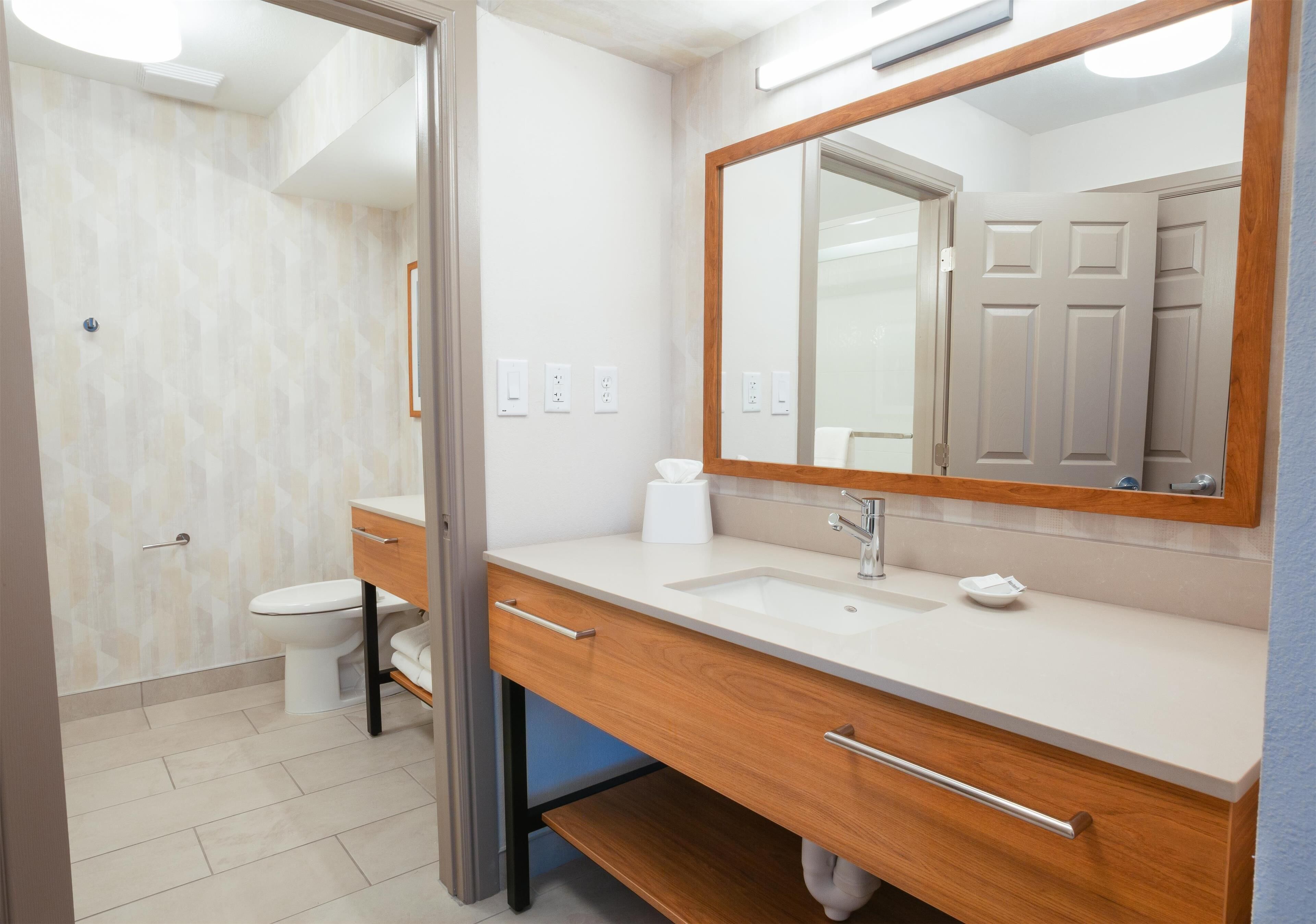 A modern bathroom with a white toilet, a wooden vanity with a sink, and a large mirror.