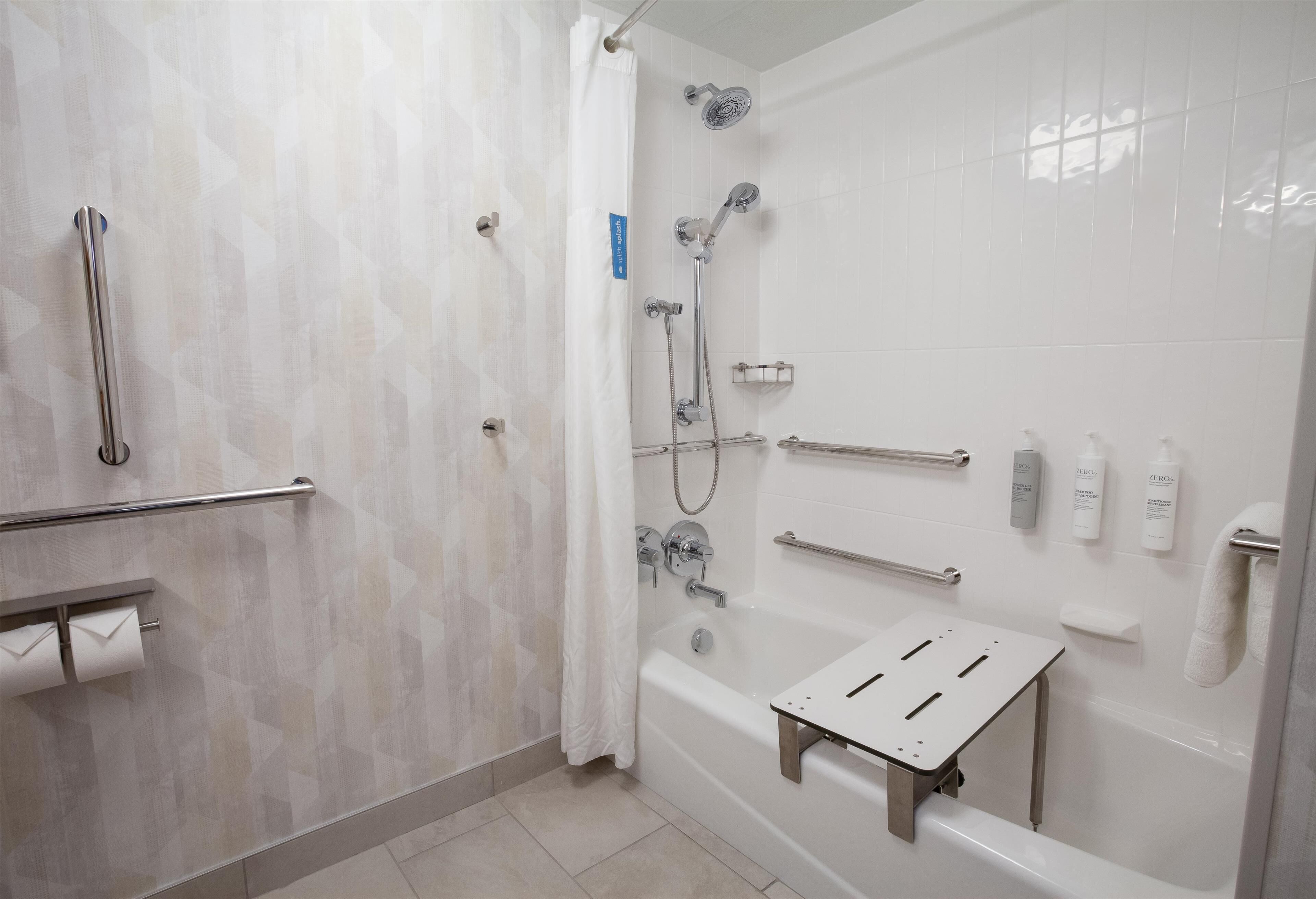 A modern bathroom with a walk-in shower, grab bars, a bathtub with a seat, and toiletries on the wall.