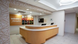 A reception desk with a 'Welcome to Hampton' sign, a modern ceiling design, and a clean, tiled floor.