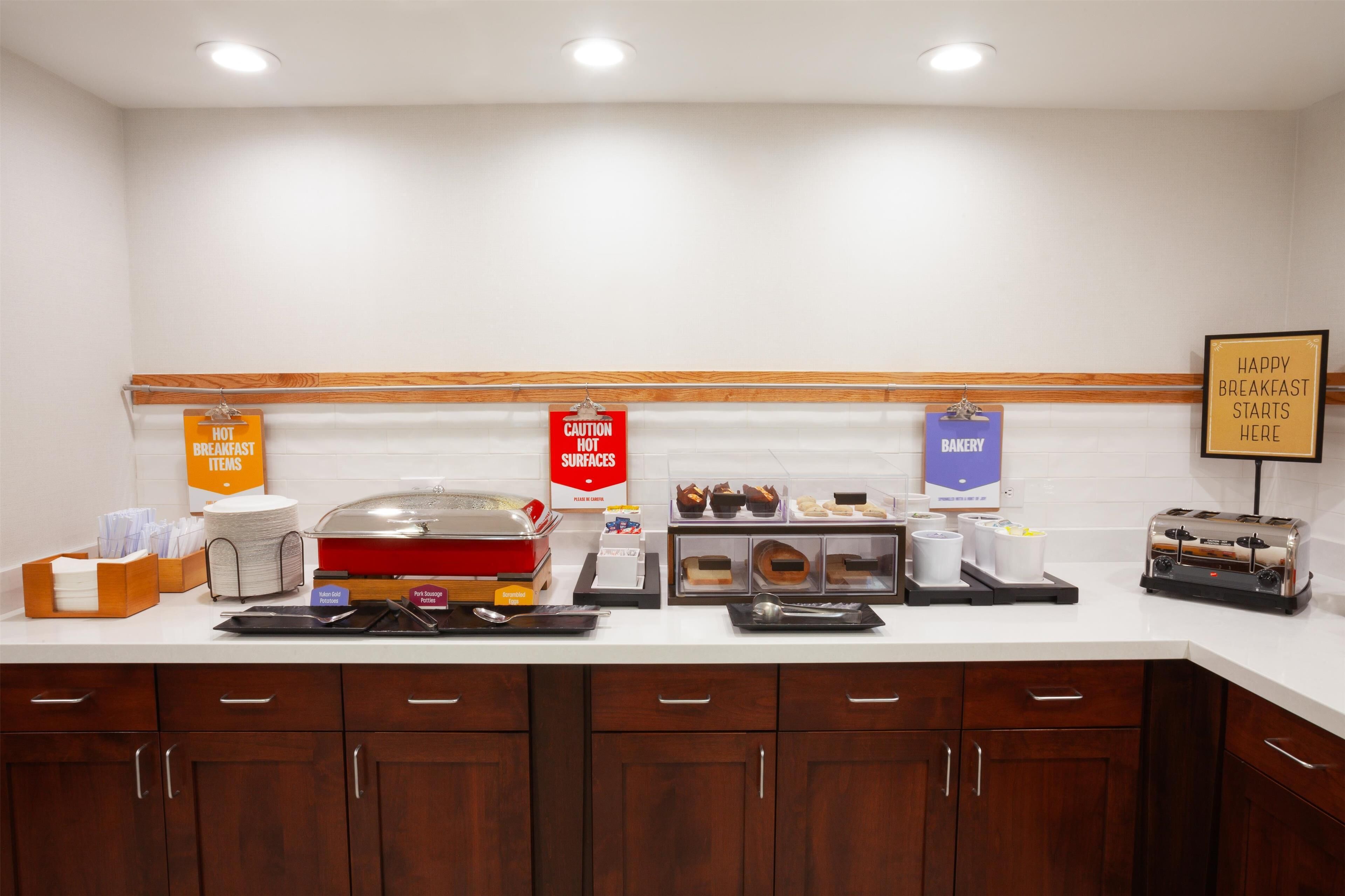 A breakfast buffet area with labeled food stations, including hot cereal, pastries, and a bakery section.
