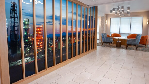A modern hotel room with a cityscape view through large windows, a dining area with orange chairs, and a chandelier.