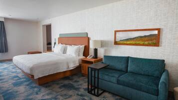 A hotel room with a bed, a sofa, a nightstand with a lamp, and a framed picture on the wall.
