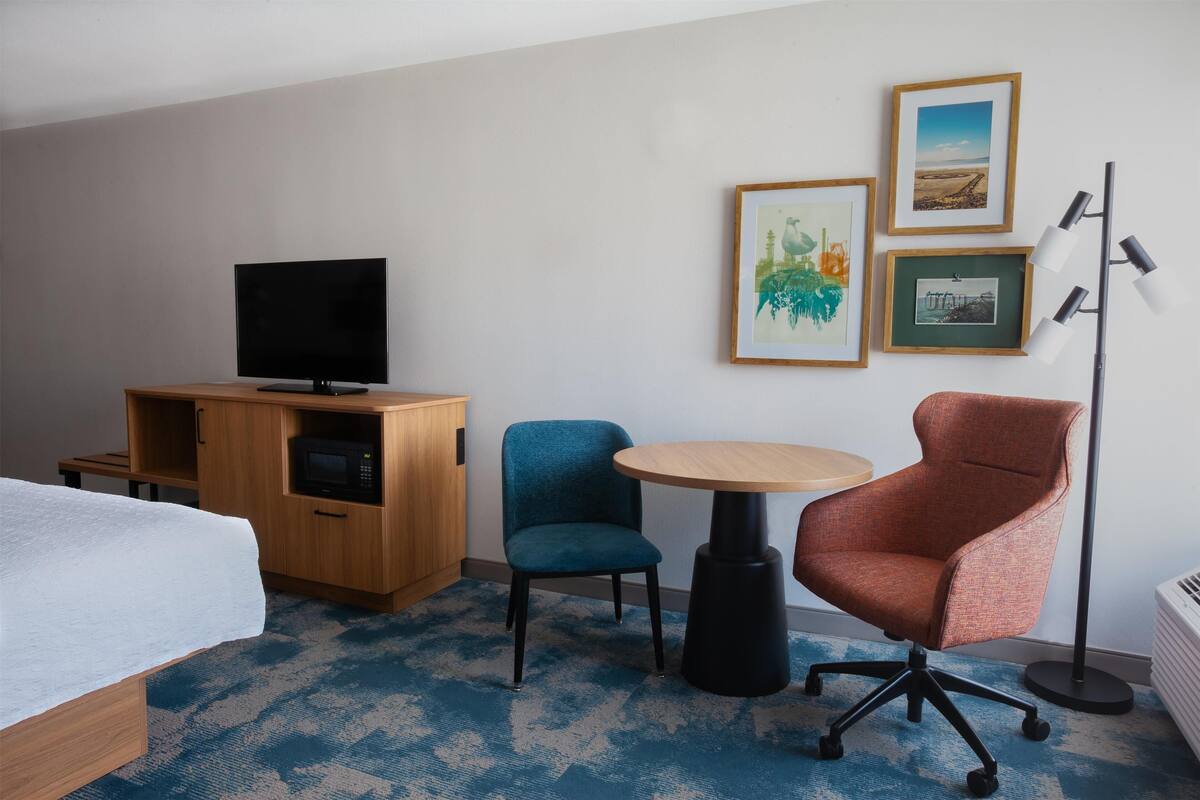 A hotel room with a bed, a TV, a microwave, a round table, two chairs, and framed pictures on the wall.