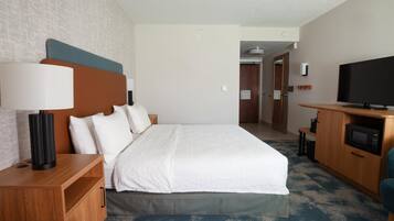 Una habitación de hotel con cama, mesita de noche, lámpara, televisor y microondas.