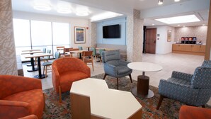 A hotel lobby with seating areas, a coffee station, and a TV mounted on the wall.
