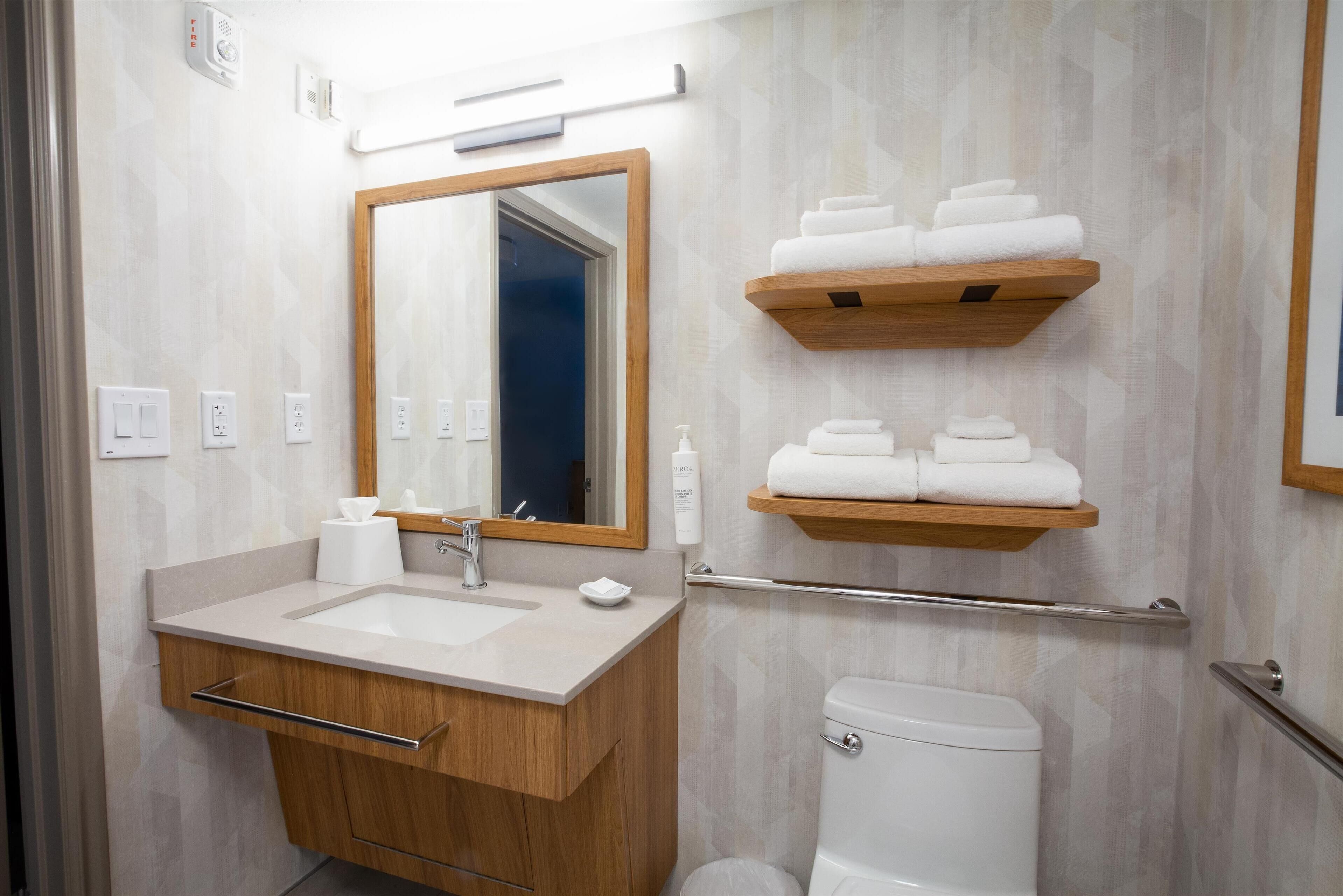 A modern bathroom with a wooden vanity, a large mirror, a toilet, and two towel racks.