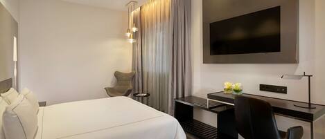 Habitación de hotel moderna con una cama grande, un escritorio con una silla, un televisor de pantalla plana y una pequeña mesa con flores.