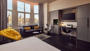 Una habitación de hotel moderna con una cama grande, un sofá, una silla amarilla, un escritorio y un televisor.