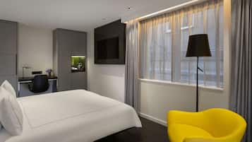 A hotel room with a bed, a desk with a chair, a TV, and a window with curtains.